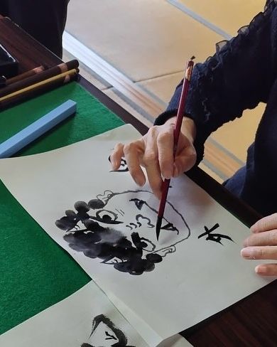 緑の毛氈の上で、墨一色で絵を描いているおけいこの手元